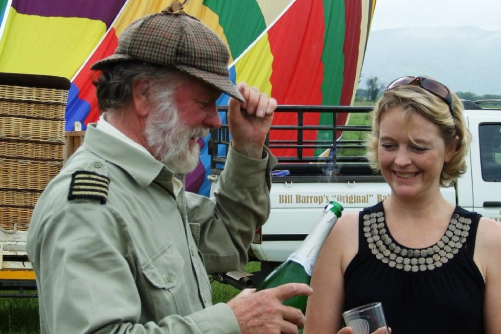 Bill Harrop preparing a sparkling wine toast beside a colourful hot air balloon