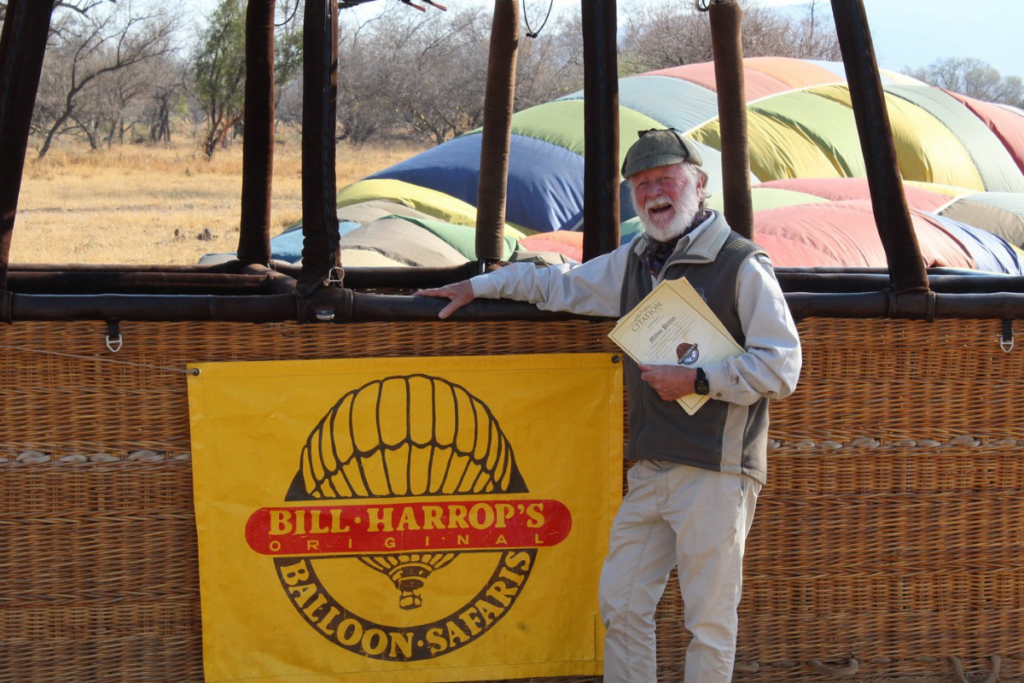 Bill Harrop holding a Certificate of Bravery beside a balloon basket and company banner